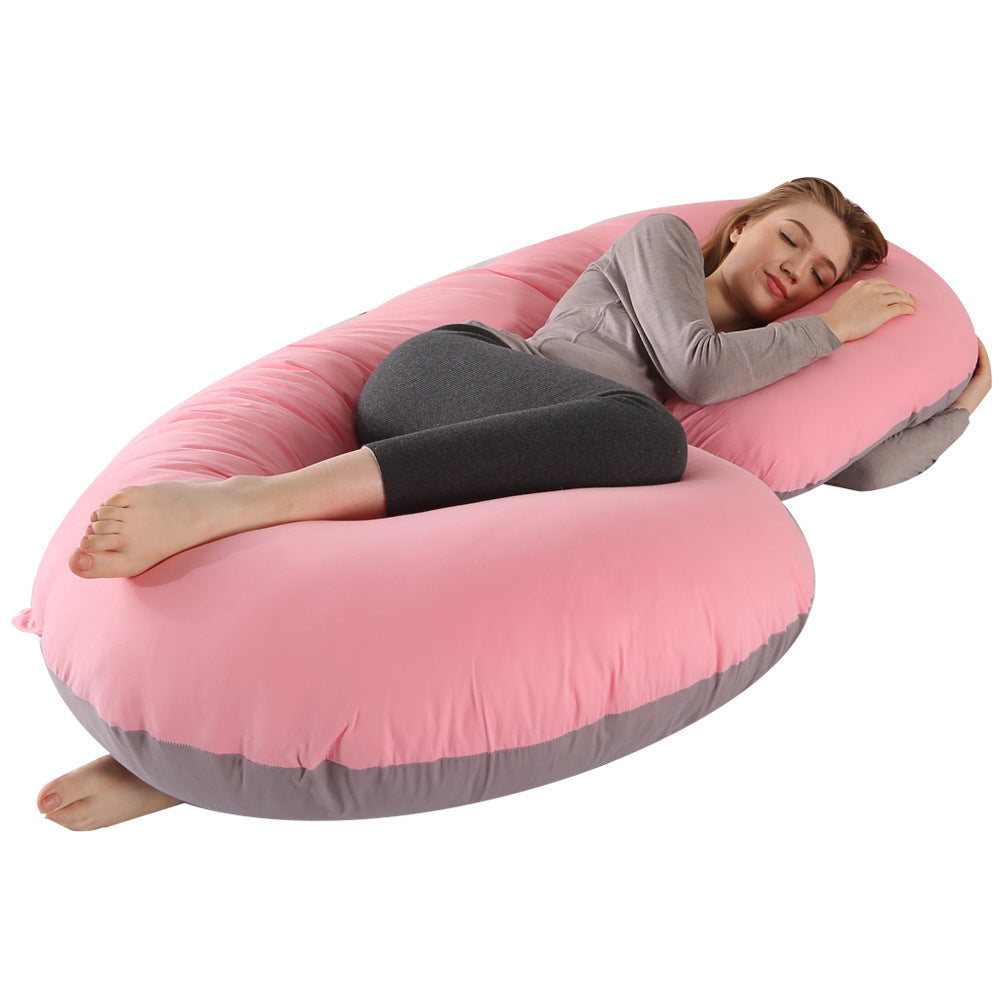 Pregnant woman sleeping soundly on a large pink and gray C-shaped velvet maternity pillow.