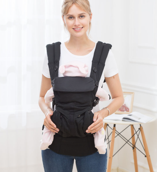Woman wearing a black ergonomic baby carrier with a doll, showcasing adjustable straps and breathable cotton.