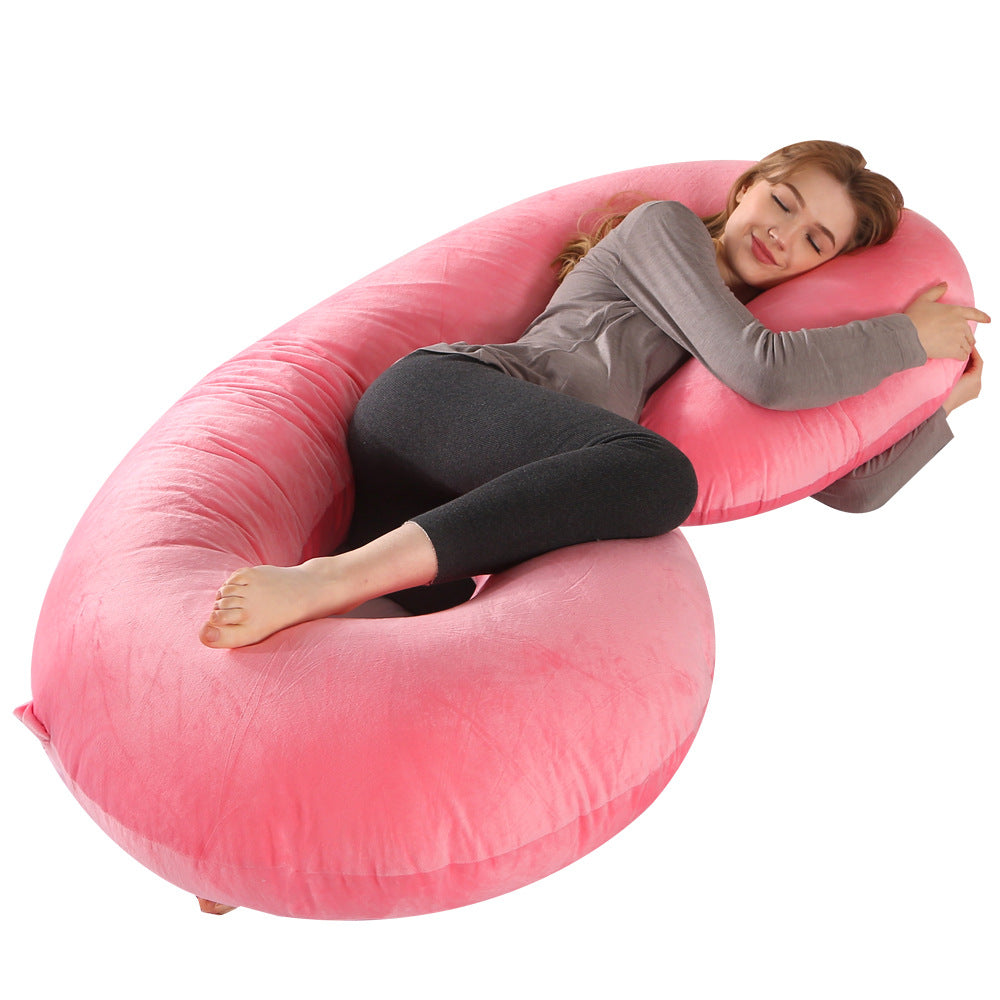 Pink velvet C-shaped pregnancy pillow supporting a woman sleeping comfortably.