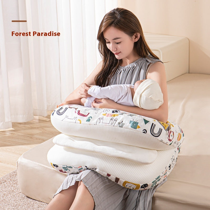 Smiling mother cradling baby on a white multi-use nursing pillow with colorful animal and letter patterns.