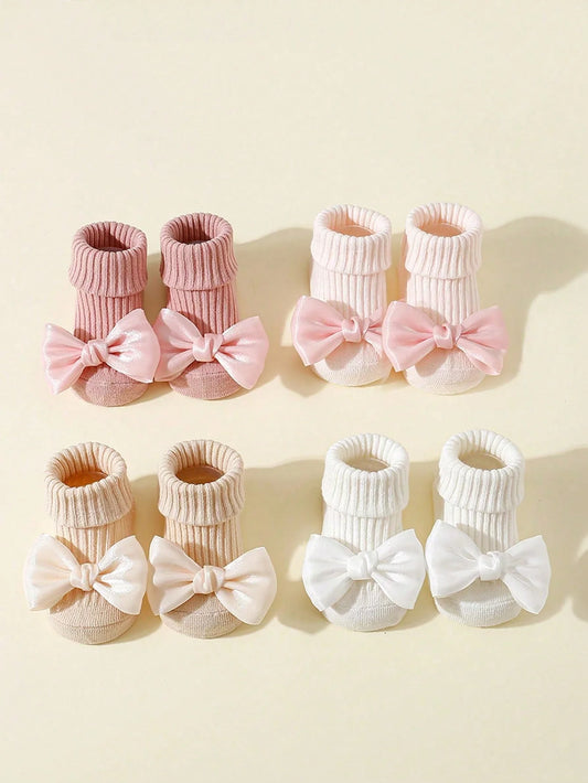 Four pairs of cotton baby socks with bows: pink, light pink, beige, and white, featuring non-slip soles.