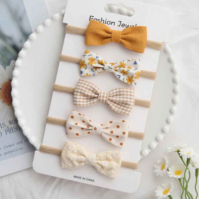 Set of 5 handmade cotton baby headbands with bows in various patterns: mustard, floral, plaid, polka dot, and embroidered cream.