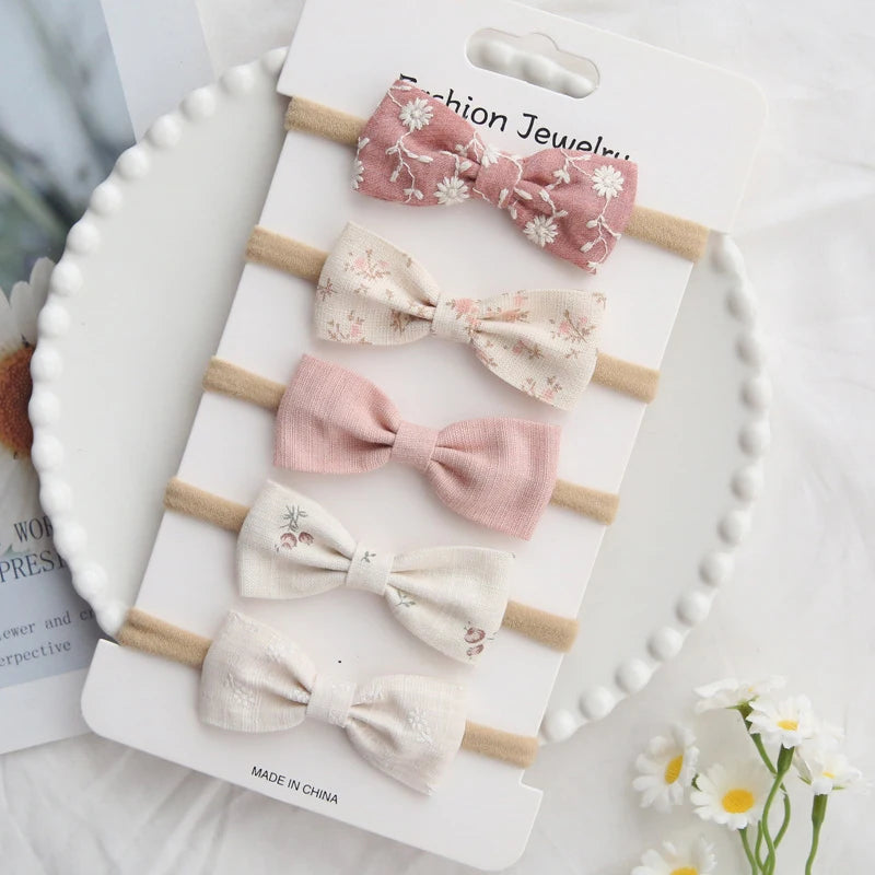 Set of five handmade cotton baby headbands with bows in pink, cream, and floral patterns.