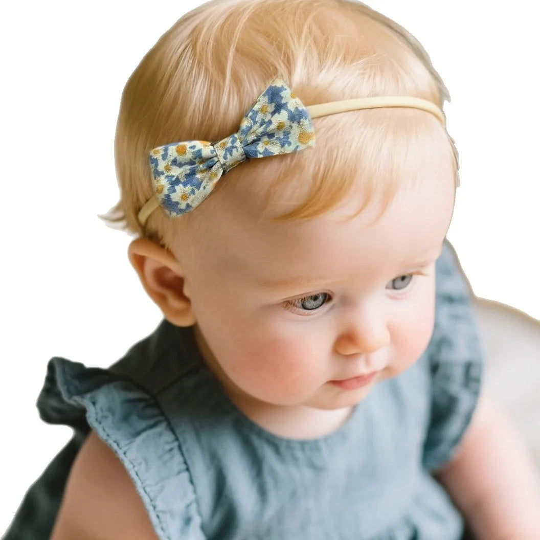 Adorable baby wearing a soft, elastic headband with a blue and yellow floral bow.