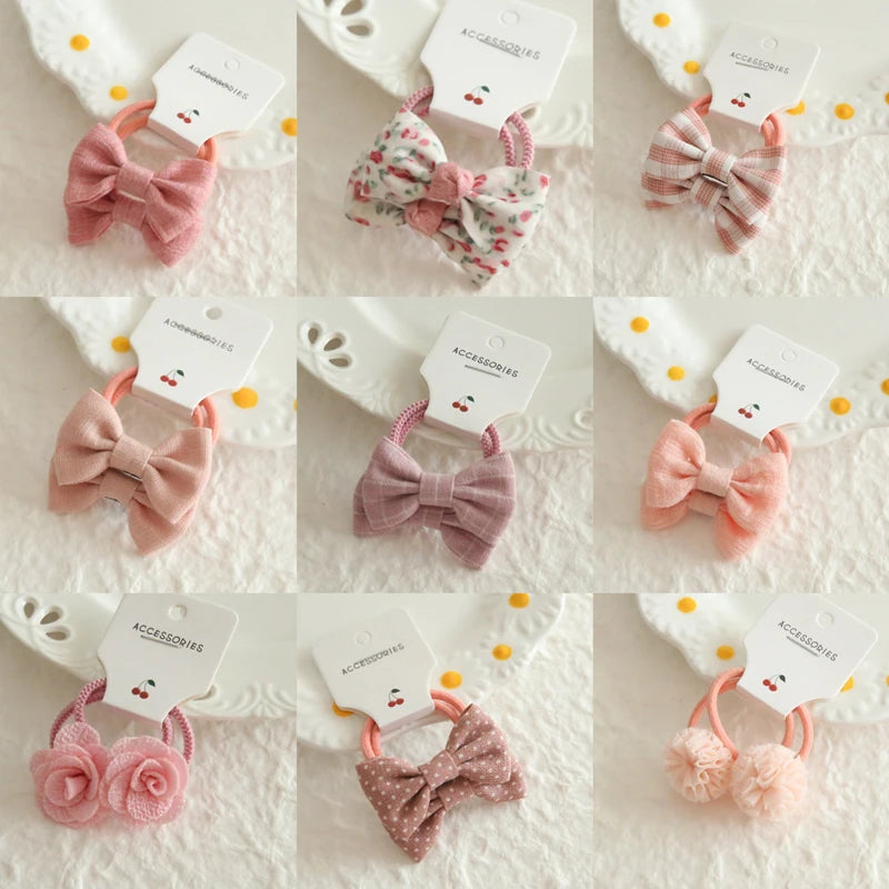 Nine soft cotton hair ties for babies and girls, featuring pink bows, floral patterns, and pom-poms.