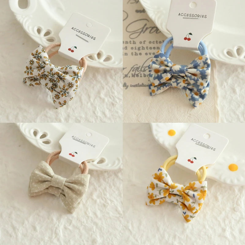 Four cotton hair ties for babies and girls, featuring bows in floral, solid beige, and yellow patterns.