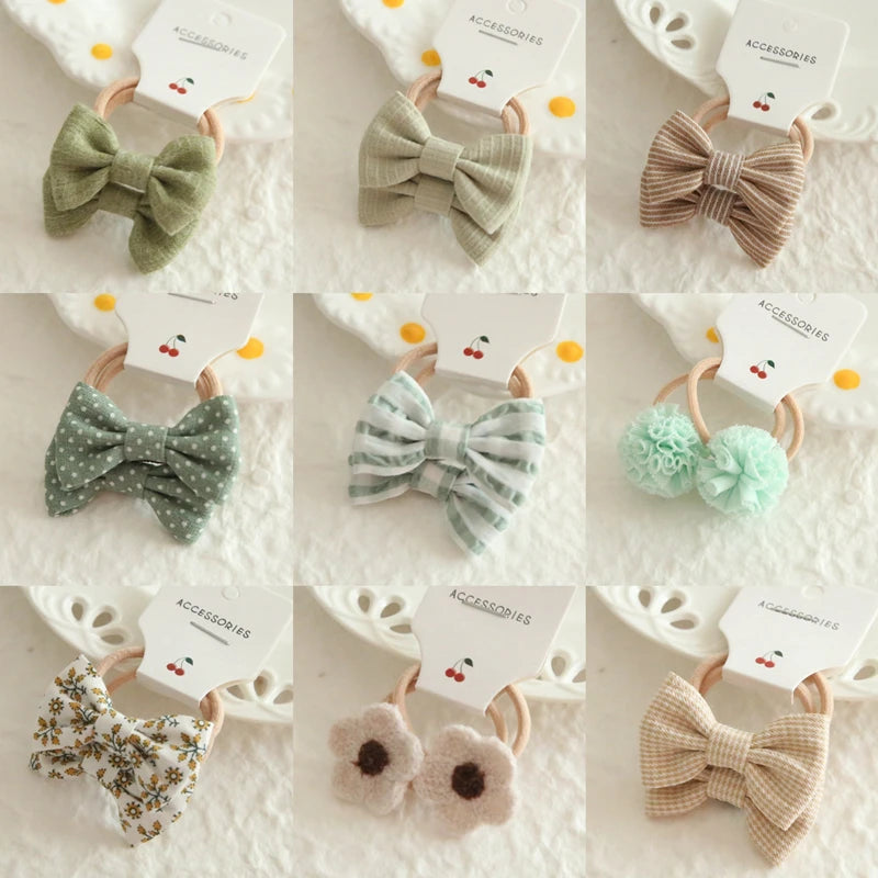 Nine soft cotton hair ties for babies and girls, featuring bows, pom-poms, and floral designs in various colors.
