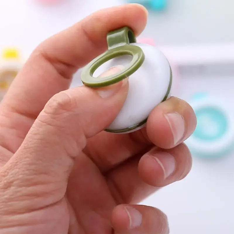 Hand holding a white, round natural mosquito repellent clip with a green plastic ring and clip.