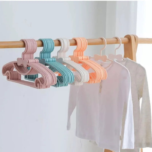Colorful macaron plastic baby clothes hangers on a wooden rack, featuring pink, blue, white, and orange.