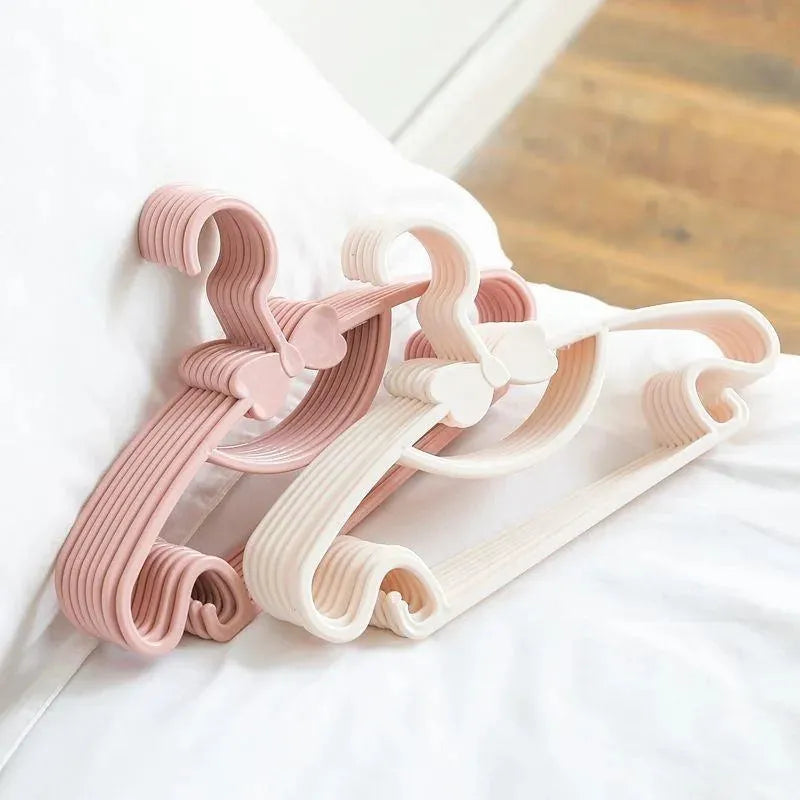 Pink and white plastic baby clothes hangers with bow details, designed for small garments.