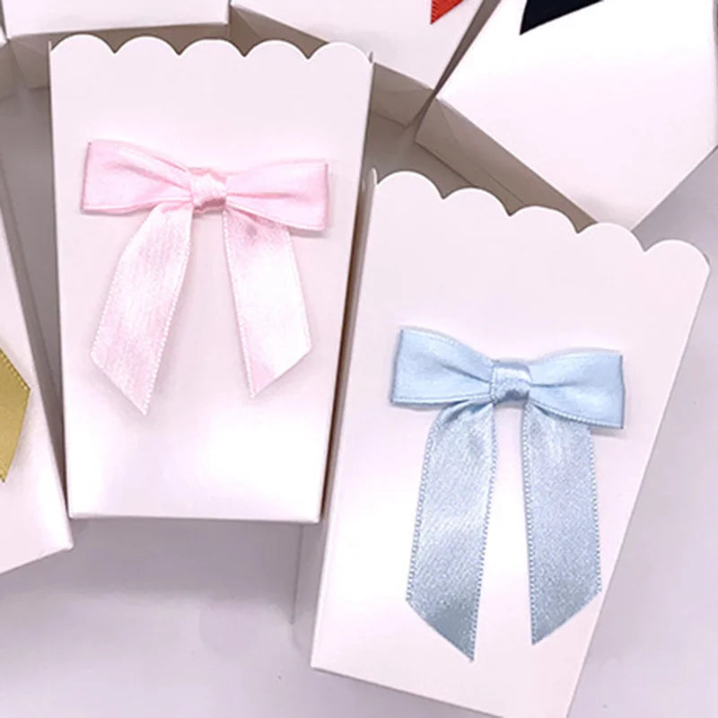 White paper party favor boxes with scalloped edges, decorated with pink and blue satin bows.