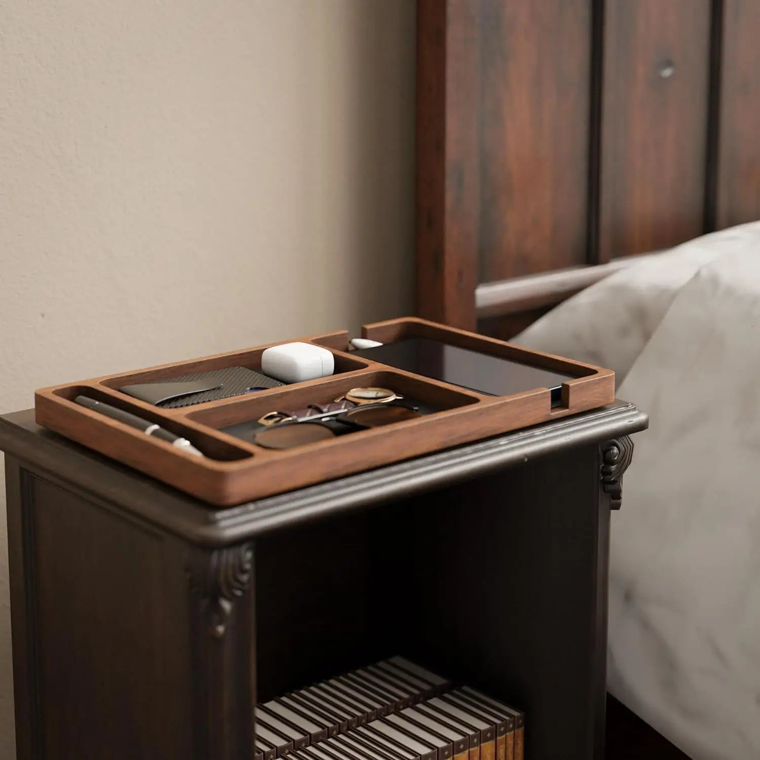 Wooden desk organizer with multiple compartments for phone, earbuds, and accessories on a dark nightstand.