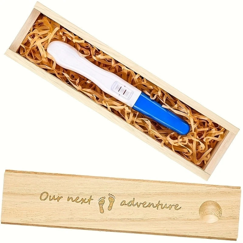 Light wood keepsake box with "Our next adventure" engraving, holding a blue and white pregnancy test on straw filler.