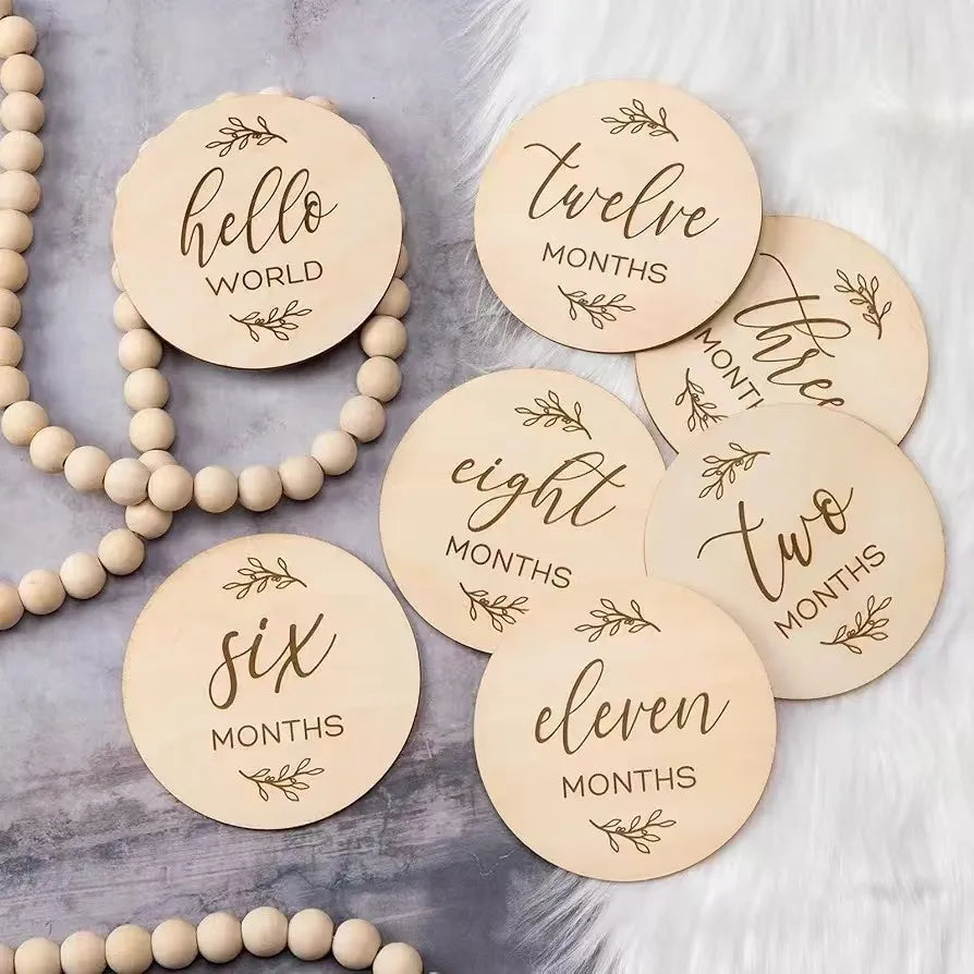 Wooden baby milestone discs with etched months and "Hello World" design, on a gray and white background.