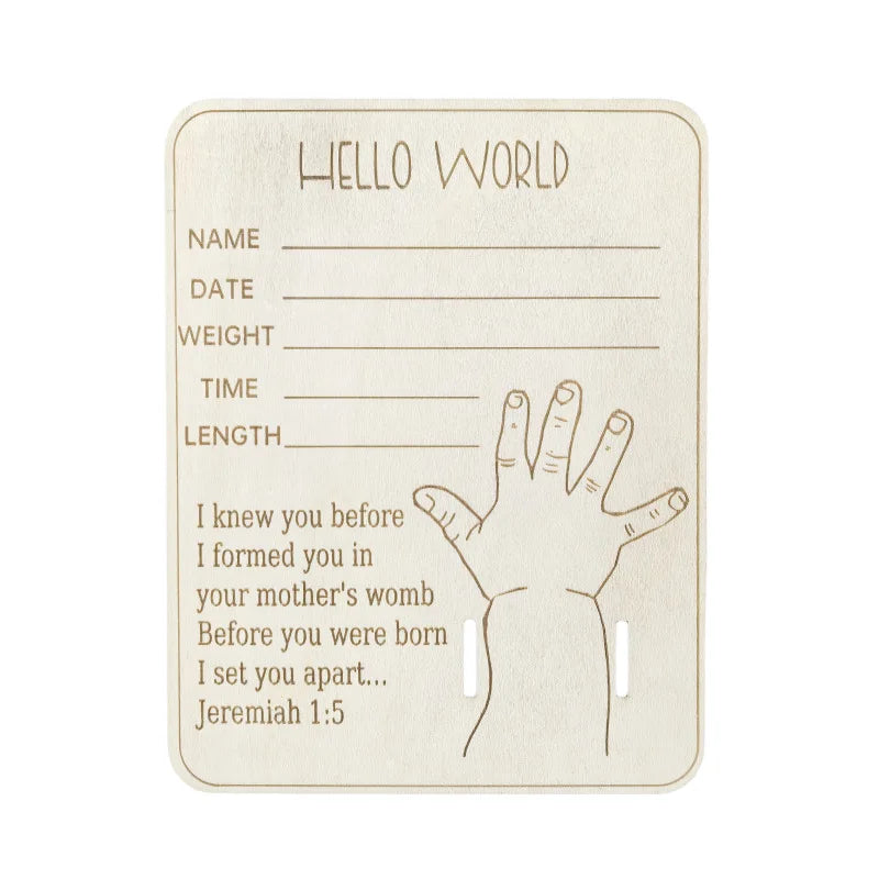 Wooden "Hello World" birth announcement plaque with baby hand illustration, lines for name, date, weight, time, length, and a Bible verse.
