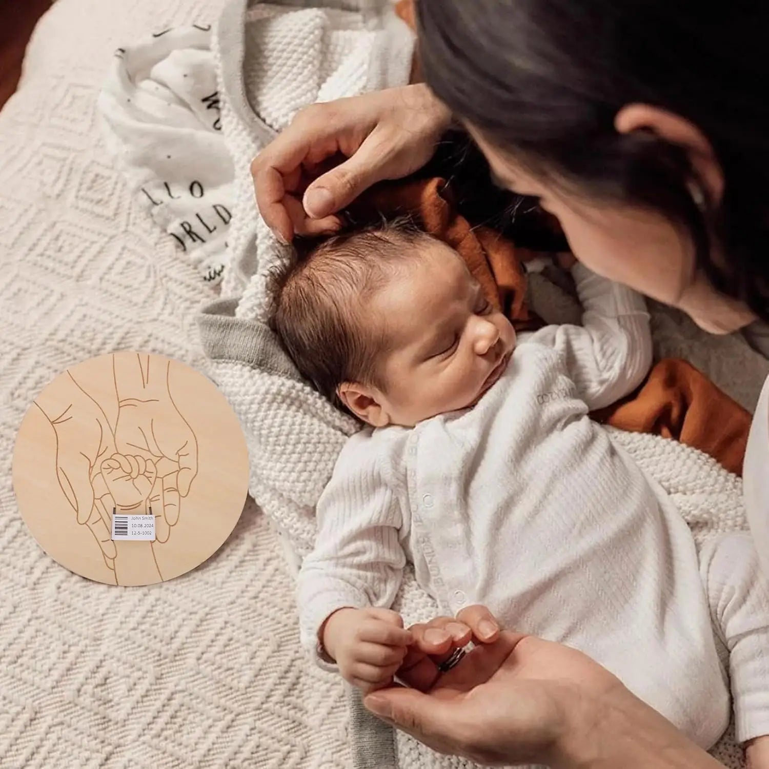 Wooden birth keepsake plaque with engraved hands, next to a sleeping newborn and parent.