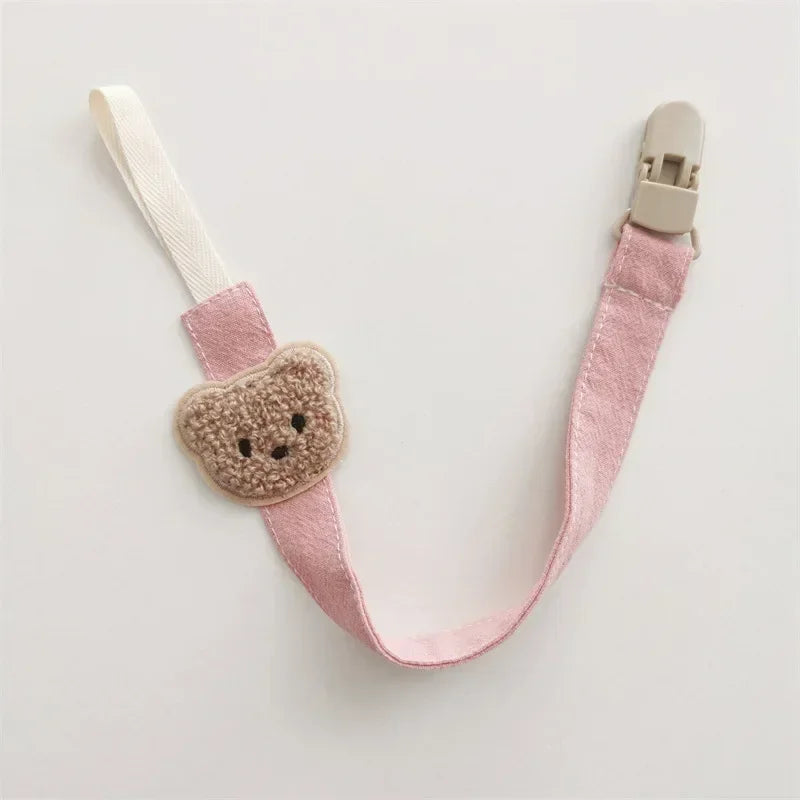 Pink cotton pacifier clip with an embroidered brown teddy bear and beige plastic clasp.