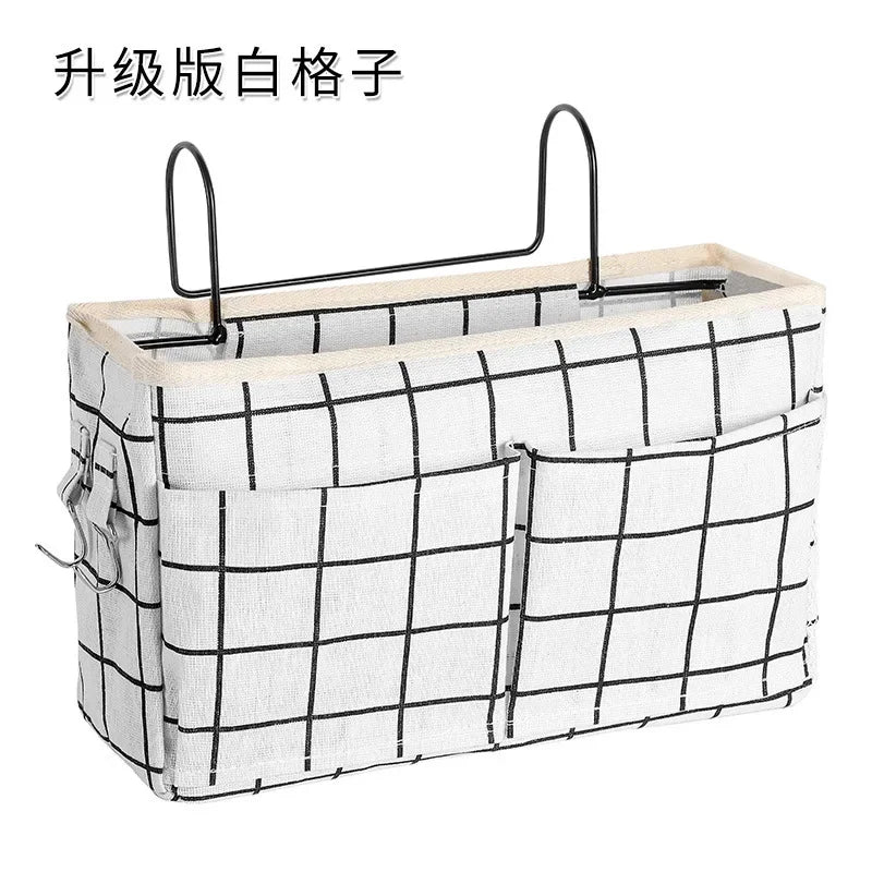 White cotton multi-pocket bedside organizer with black grid pattern and metal hooks.