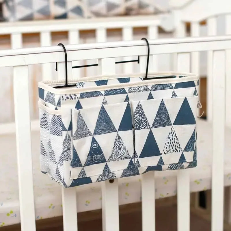 Cotton multi-compartment baby crib organizer with blue and white triangle pattern, hanging on a white crib.