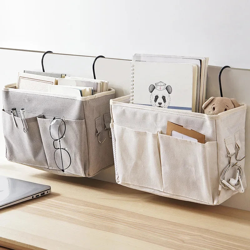 Two multi-compartment cotton blend bedside caddies, one grey and one cream, hanging with books and items.