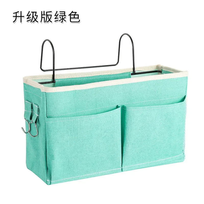 Green multi-compartment cotton fabric bedside organizer with metal hooks for baby essentials.