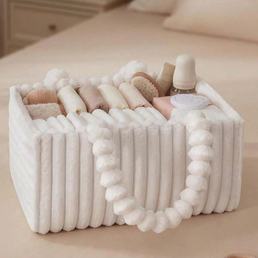 Soft white flannel diaper caddy with dividers, filled with baby essentials, on a light bed.