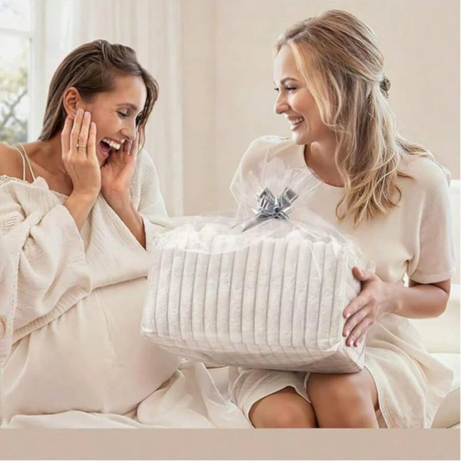 Woman gifting a large, clear-wrapped package of white diapers to a smiling pregnant woman.