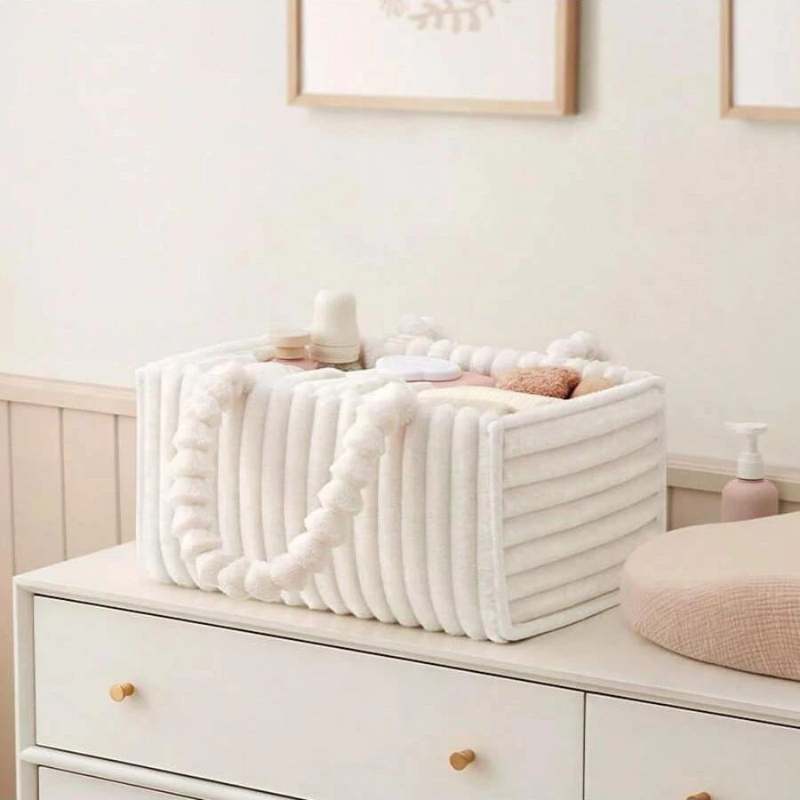 White flannel diaper caddy with soft, ribbed texture and pom-pom handles, filled with baby essentials.