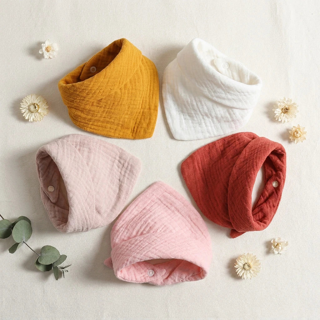 Set of 5 soft cotton baby bibs in mustard, white, light pink, dark pink, and rust with snap closures.