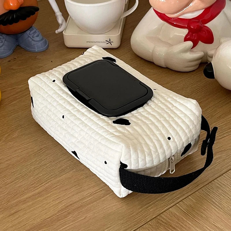 Quilted white cotton tissue and wipe dispenser with black spots, a black lid, and a hanging strap.
