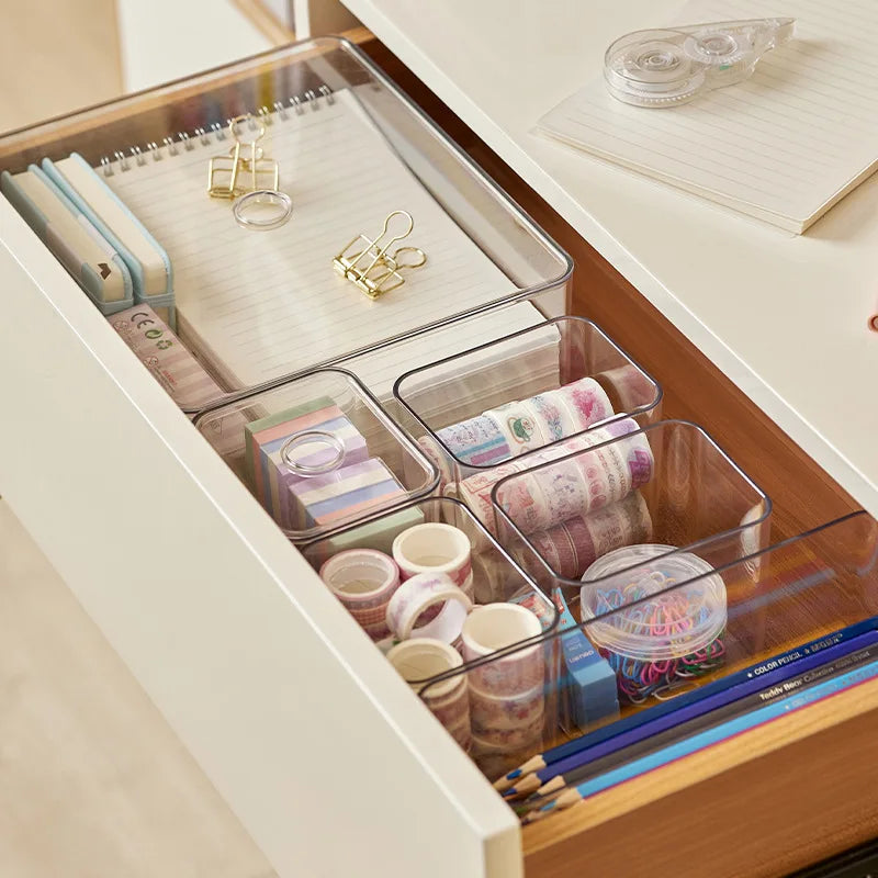 Clear acrylic drawer organizers for desk supplies like notebooks, tape, and pencils.