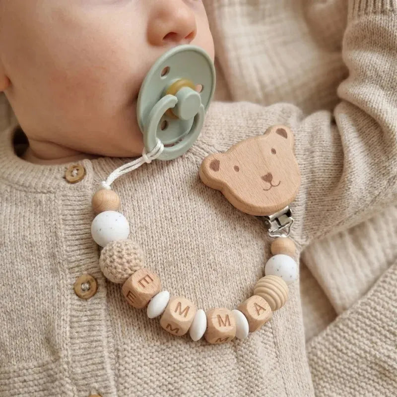 Baby with personalized wood and silicone pacifier clip featuring a bear and "EMMA" beads.