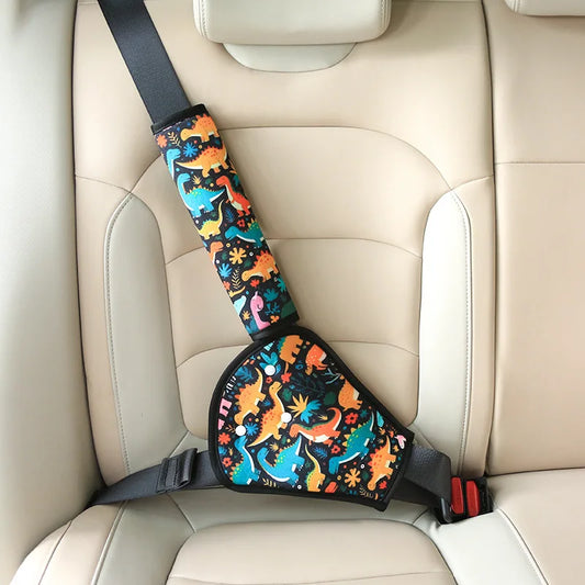 Colorful dinosaur-patterned car seat belt adjuster and shoulder pad for children, shown on a beige car seat.
