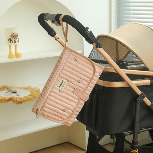 Pink quilted portable changing pad with leaf print, hanging from a stroller handle.