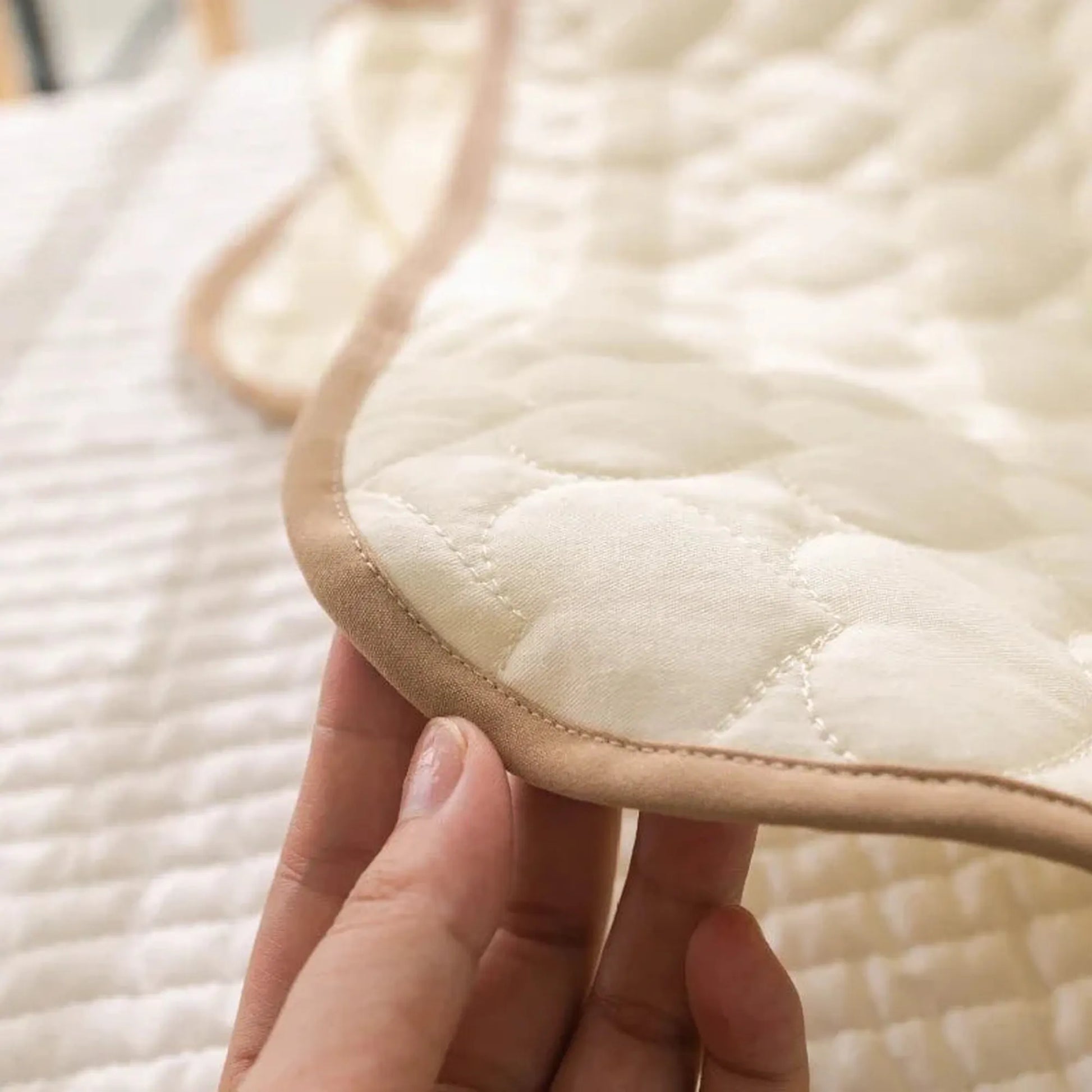 Close-up of a hand holding a quilted, off-white portable changing pad with a beige trim.