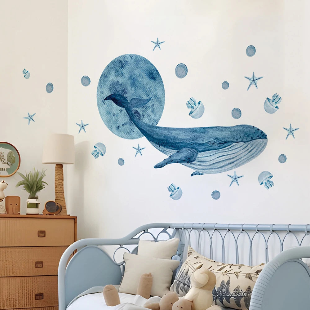 Watercolor blue whale and sea creature wall decals on a white wall above a child's bed.