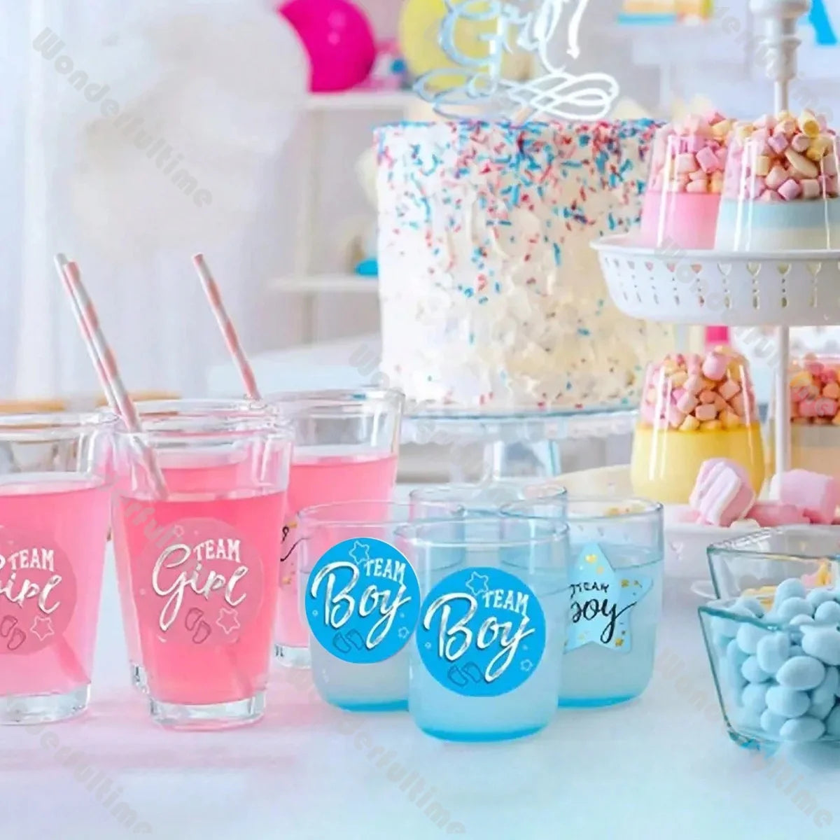 Pink "Team Girl" and blue "Team Boy" stickers on glasses at a gender reveal party with cake and treats.