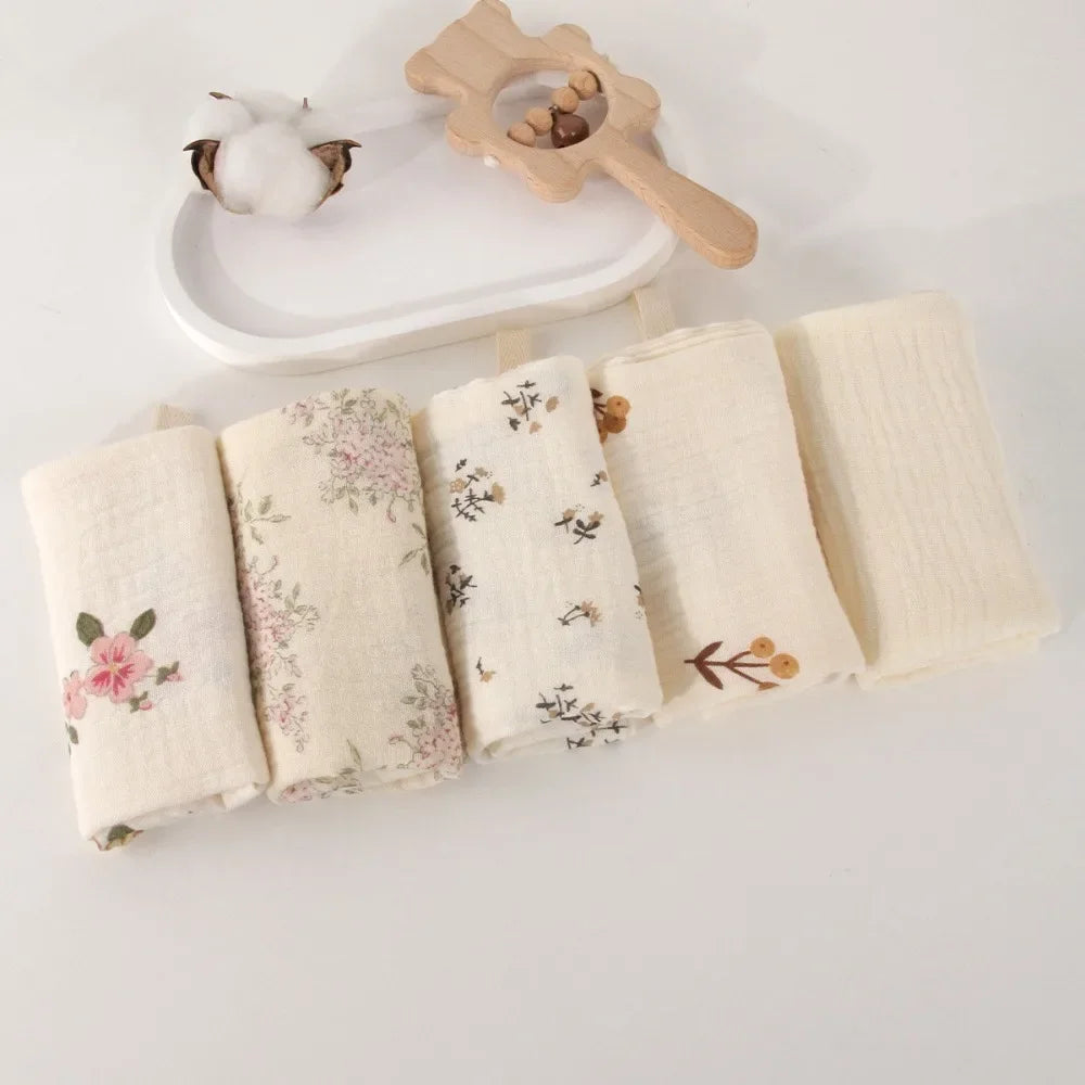 Soft cotton gauze baby towels in a 5-pack, featuring various floral prints and solid cream designs.