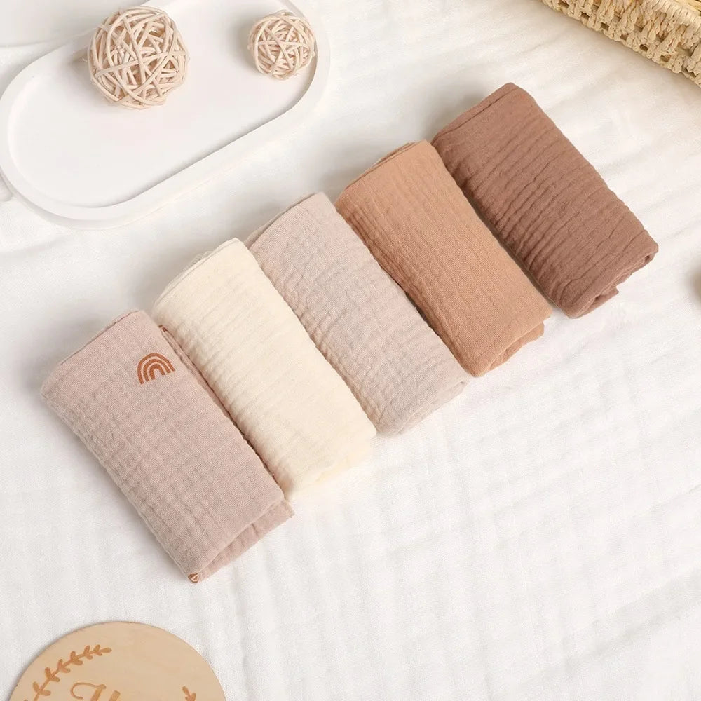 Soft cotton gauze baby towels in neutral shades of beige, cream, and brown, one with a rainbow design.