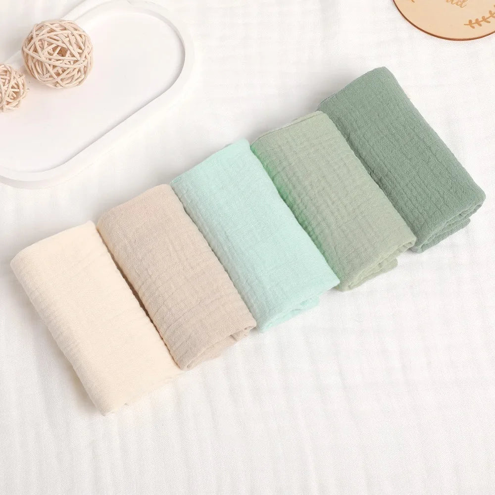 Soft 100% cotton gauze baby towels in natural, beige, mint, and sage green shades, folded neatly.