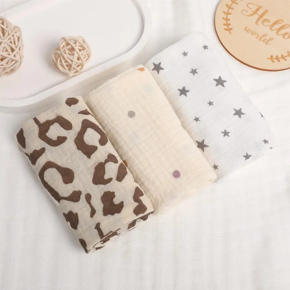 Three soft 100% cotton gauze baby towels: leopard print, cream with dots, and white with gray stars.