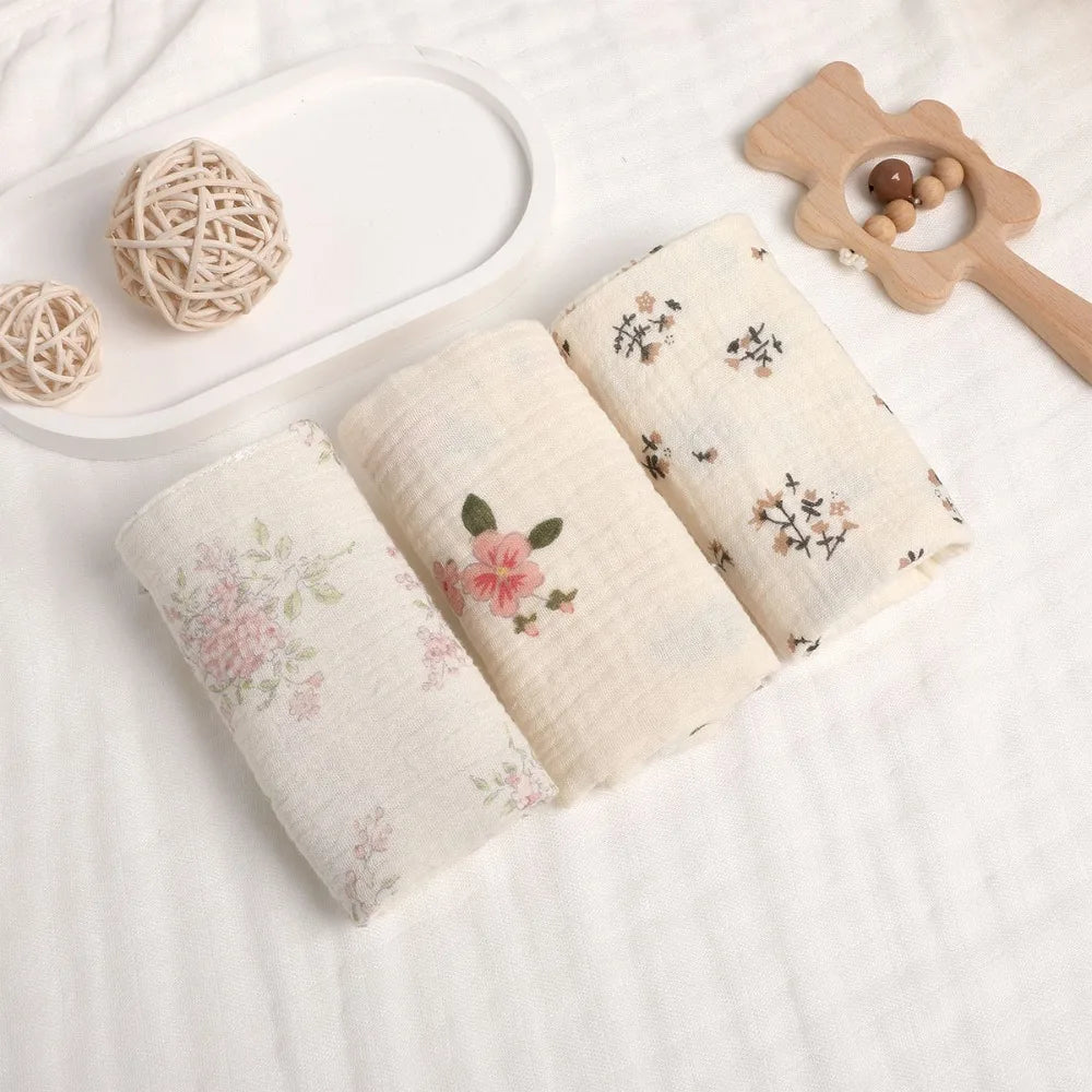 Three soft, off-white 100% cotton gauze baby towels with delicate floral patterns.