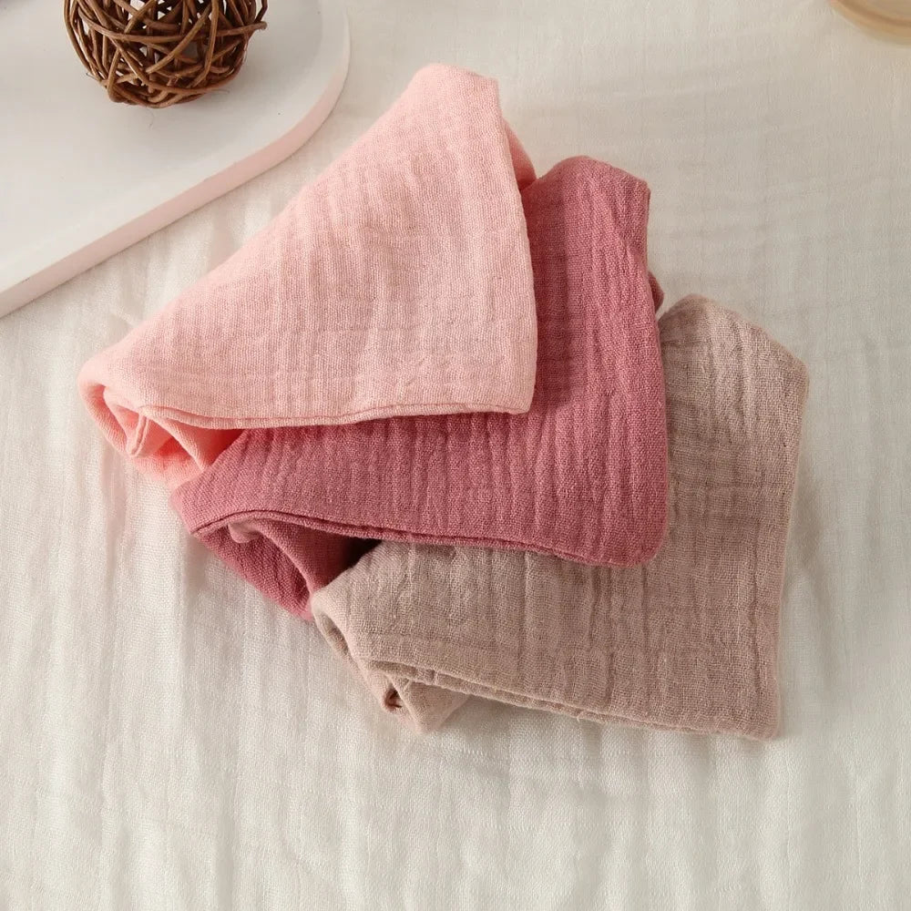 Three folded soft 100% cotton gauze baby towels in shades of pink and beige.