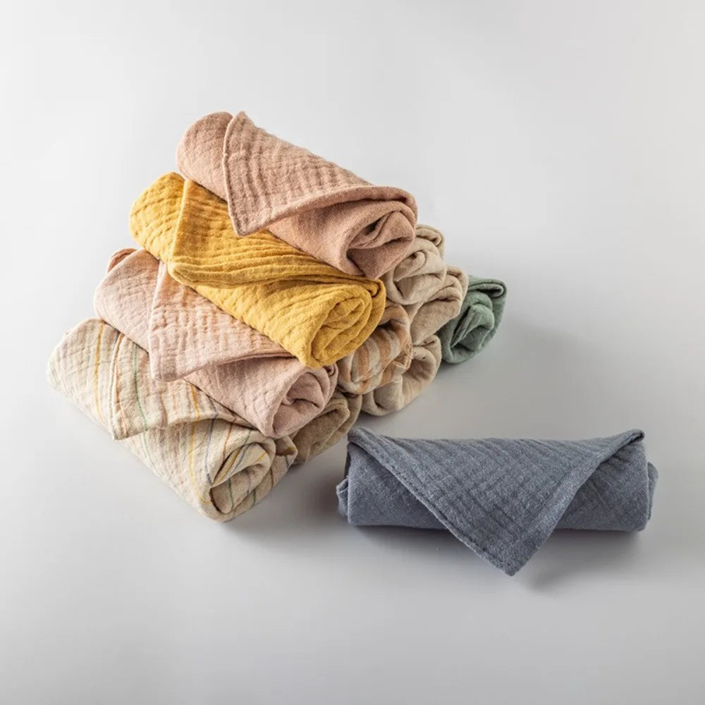 Soft multi-colored 100% cotton gauze baby towels, stacked and rolled, on a white background.