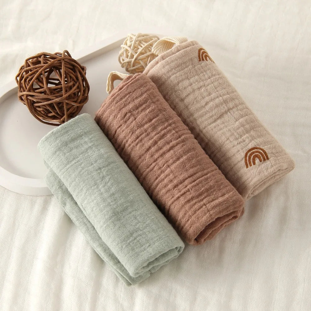 Soft 100% cotton gauze baby towels in sage green, terracotta, and beige with rainbow embroidery.