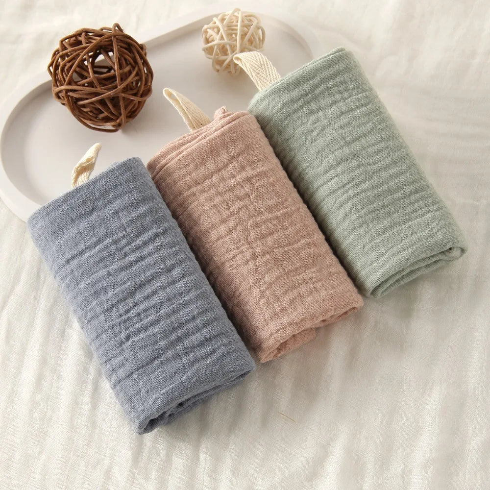 Three soft, textured 100% cotton gauze baby towels in blue, pink, and green, with hanging loops.