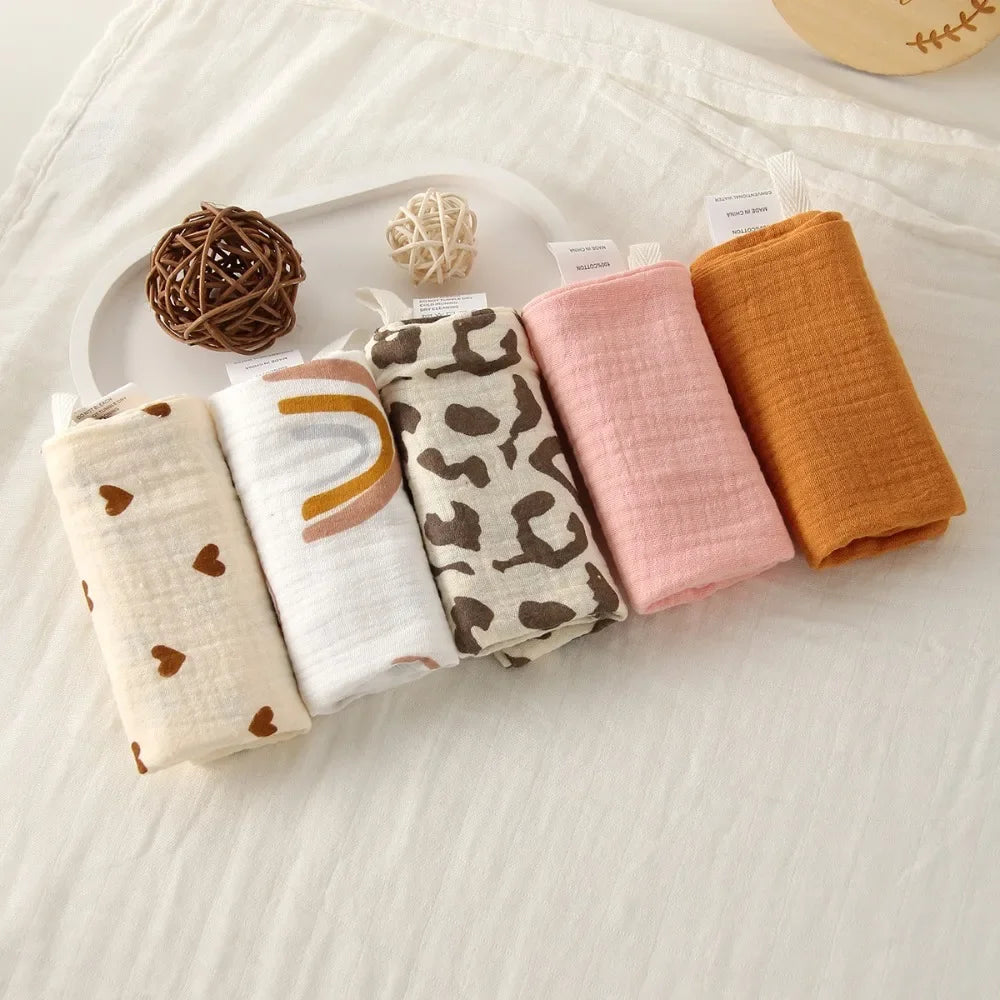 Five rolled baby gauze cotton towels in assorted colors and patterns: hearts, rainbow, leopard, pink, and orange.