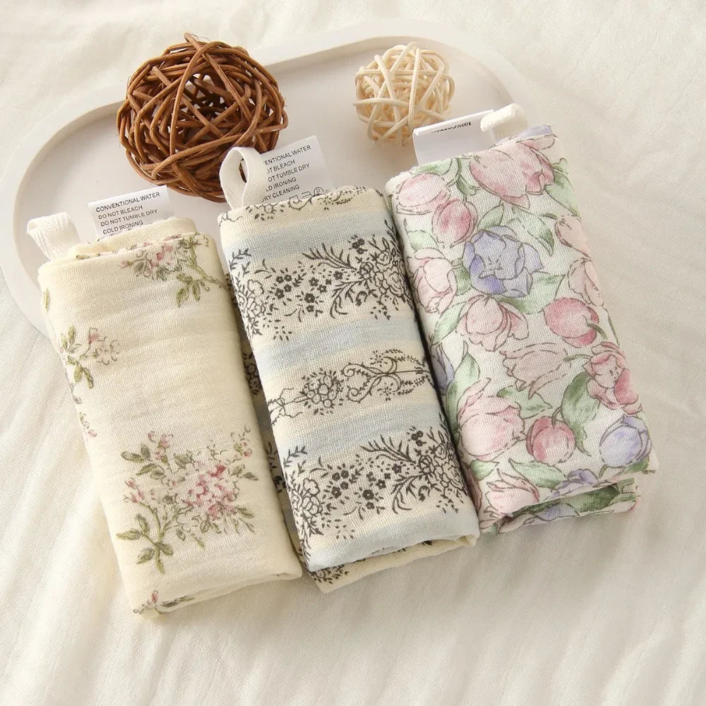 Three rolled soft cotton gauze baby towels with floral patterns, on a white tray.
