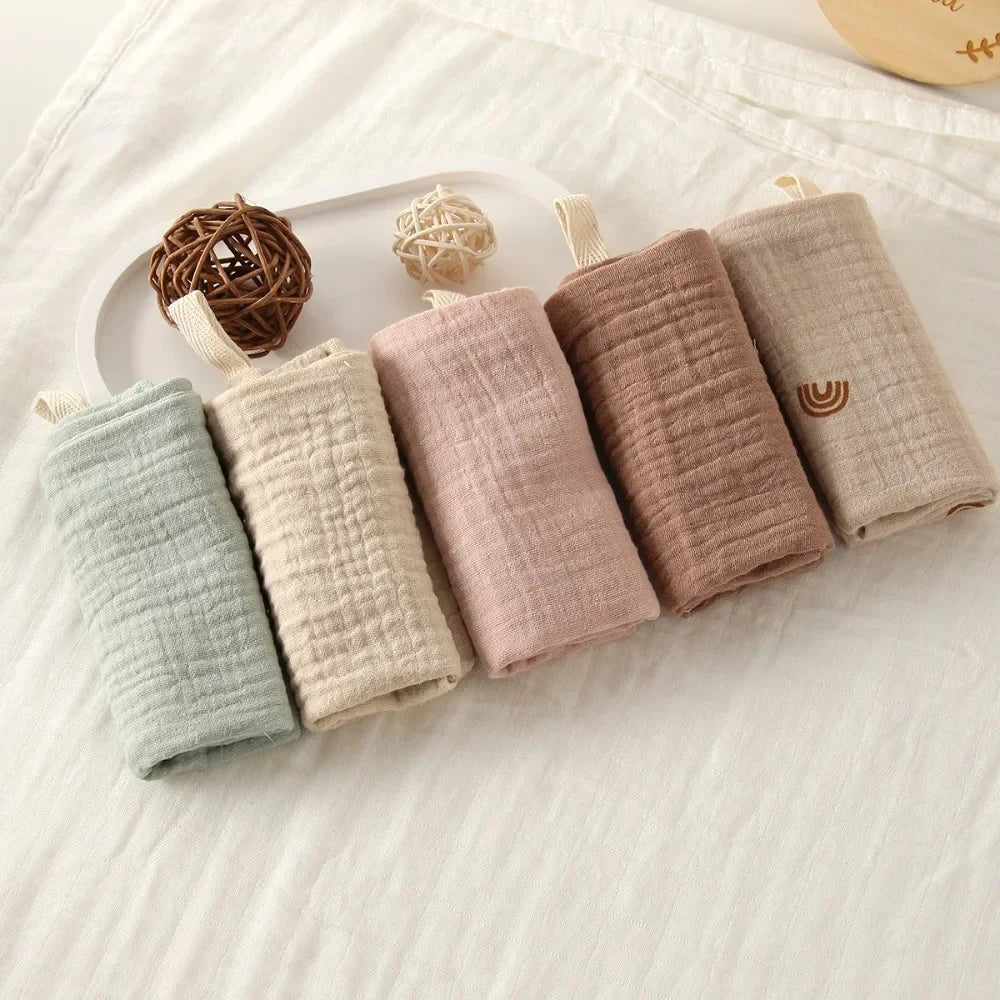 Soft 100% cotton gauze baby towels in pastel shades of blue, cream, pink, brown, and beige.