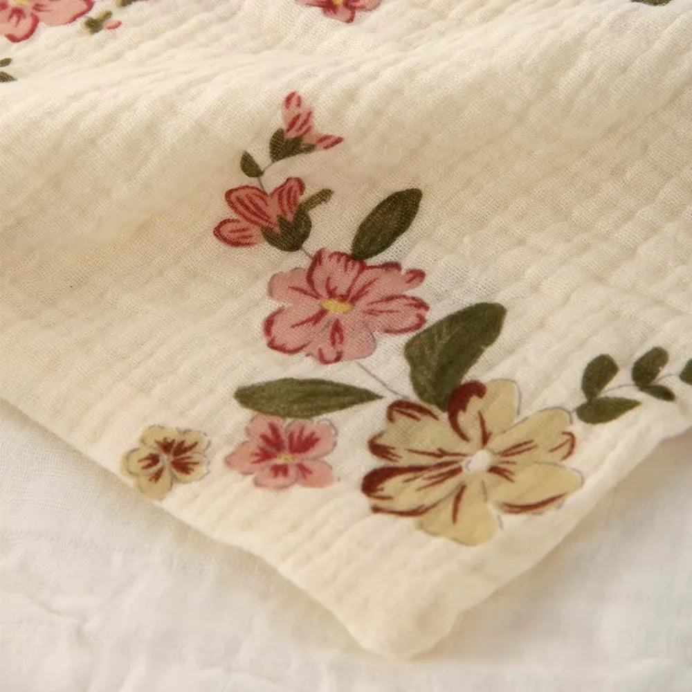 Close-up of a soft, cream-colored 100% cotton gauze baby towel with delicate pink and yellow floral embroidery.